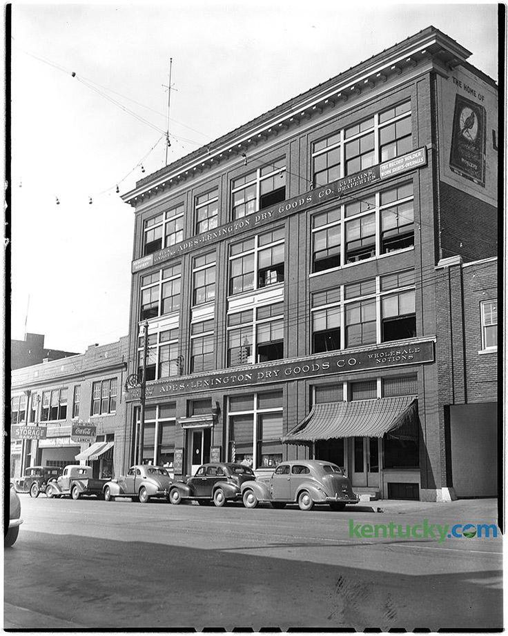 an old black and white photo of cars parked in front of a building with many windows