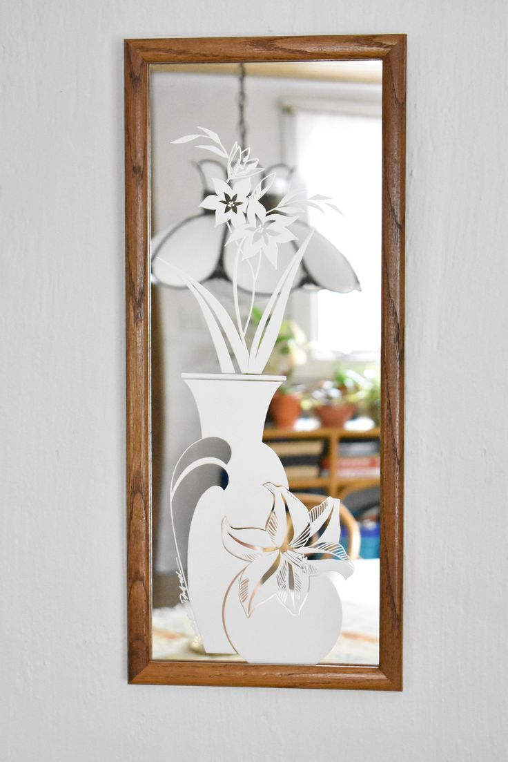 a white vase with flowers in it is reflected in a mirror on the wall next to a table