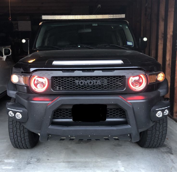 the front end of a black truck parked in a garage next to another vehicle with its lights on