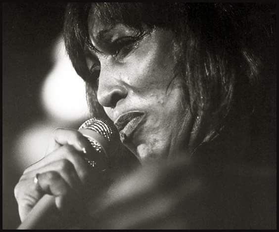 a black and white photo of a woman singing into a microphone