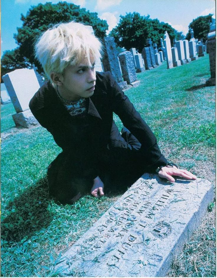 a woman sitting on the ground next to a headstone