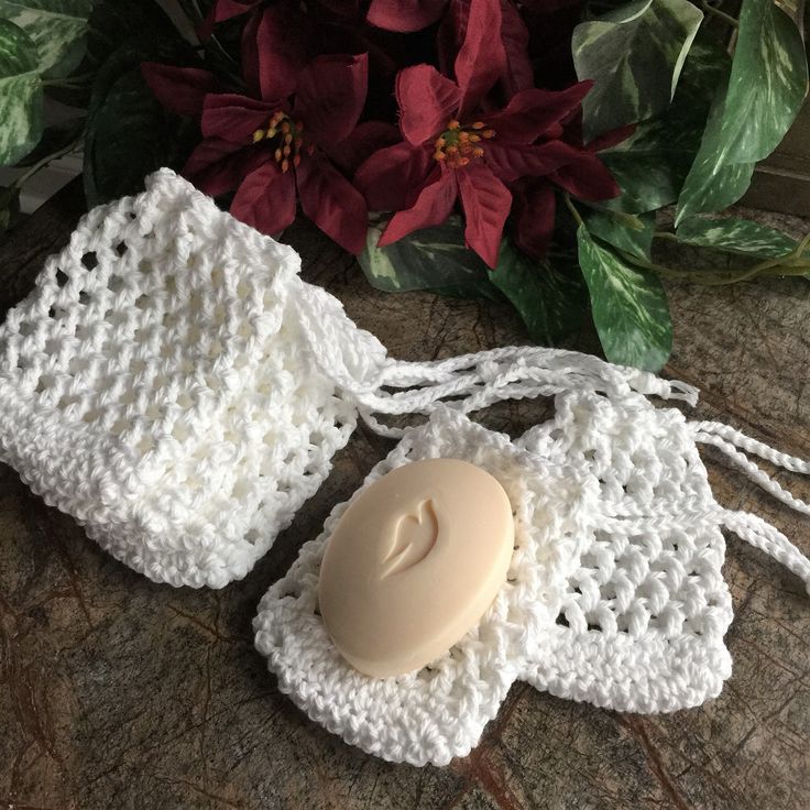 a white crochet bag with a soap in it on a table next to flowers