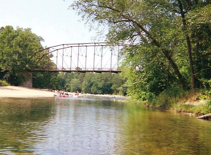 people are in boats on the river under an old bridge over which is being used as a picnic area