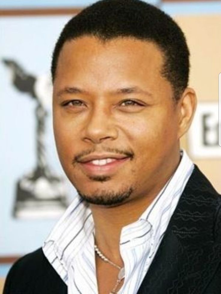 a close up of a person wearing a suit and smiling at the camera with an award in the background