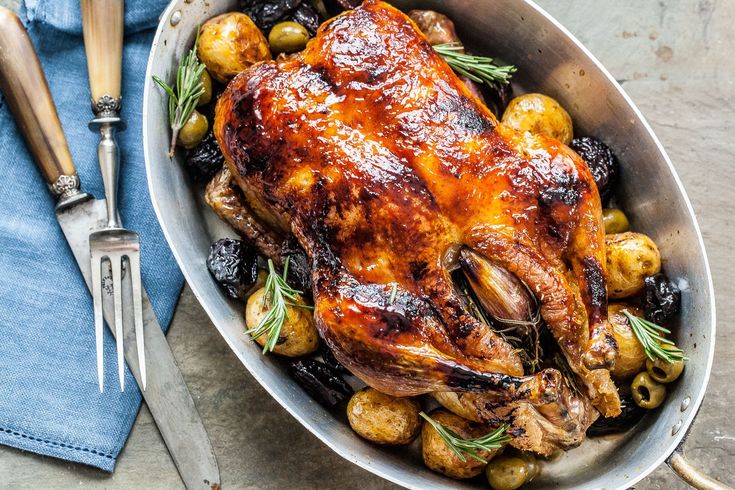 a roasting pan filled with chicken, potatoes and olives next to a fork