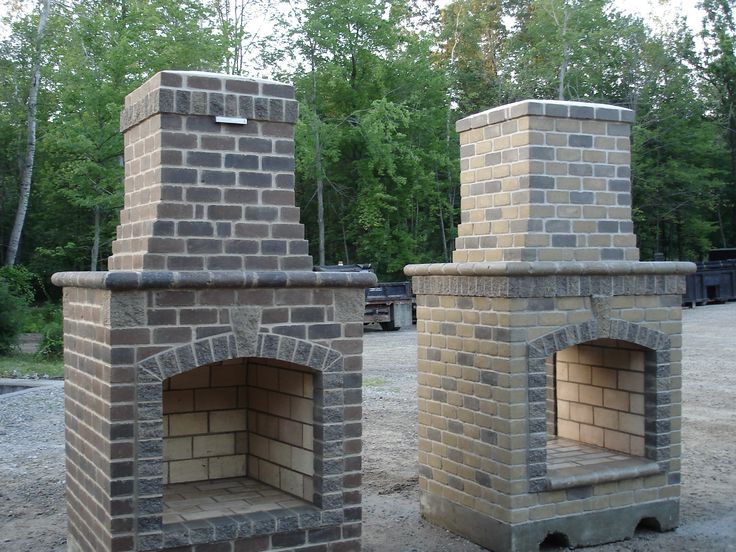 two brick ovens sitting side by side in the middle of a gravel area with trees in the background