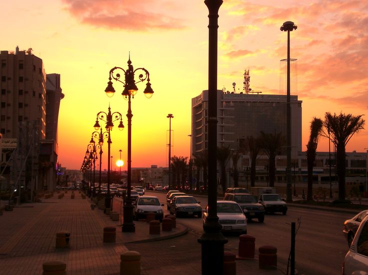 the sun is setting over a city street with many cars parked on the side walk