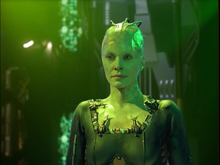 an alien woman with green hair in a dark room