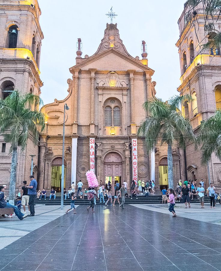 people are walking around in front of a large building with tall towers and palm trees