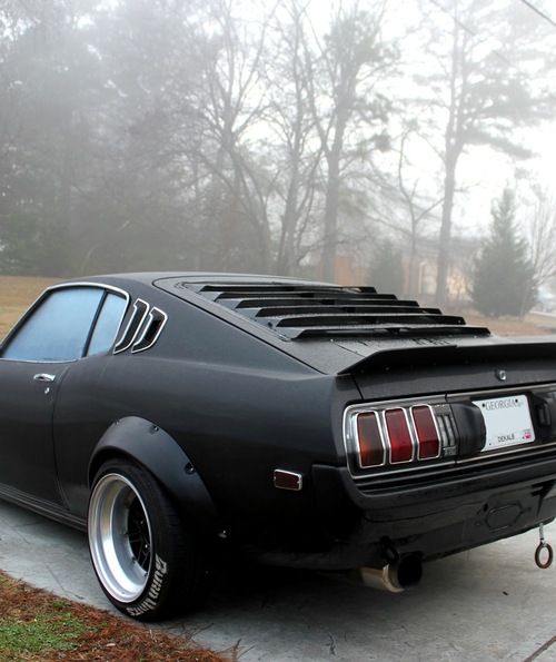 a black car parked in front of a house on a foggy day with trees behind it