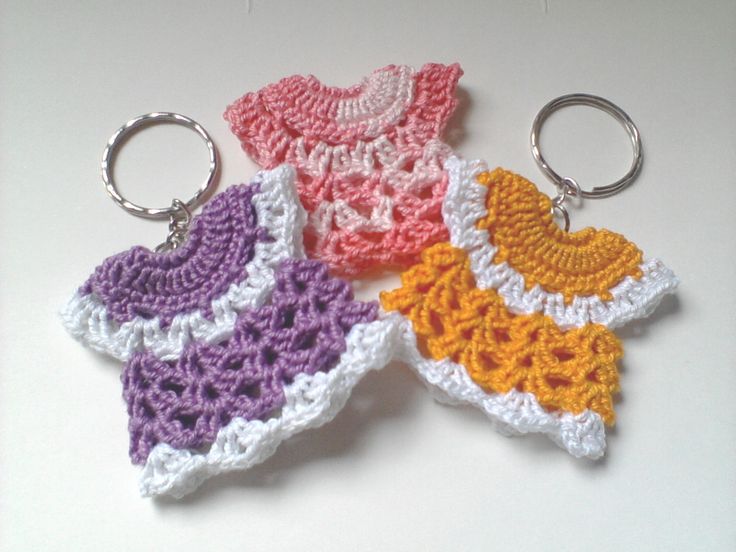 three crocheted keychains are sitting on a white surface, one is pink, one is yellow and the other is purple