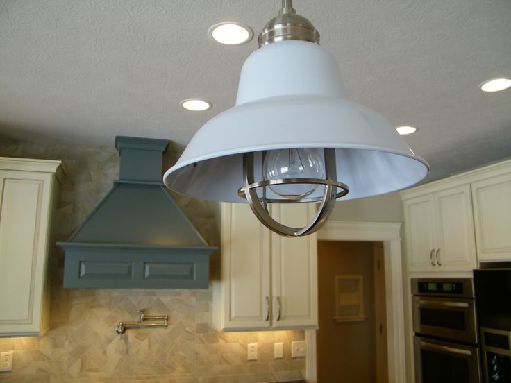 a white light hanging from the ceiling above a kitchen counter and stove top with an oven in the background