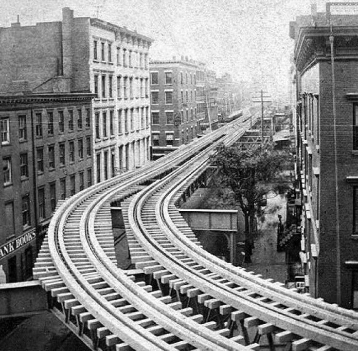 an old black and white photo of a train track in the middle of city buildings