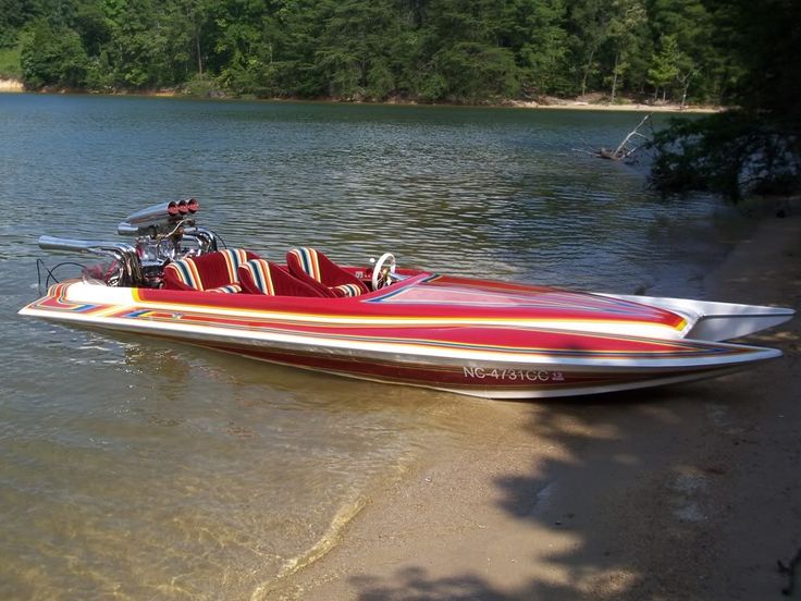 a red and white speed boat sitting on the shore of a lake with trees in the background