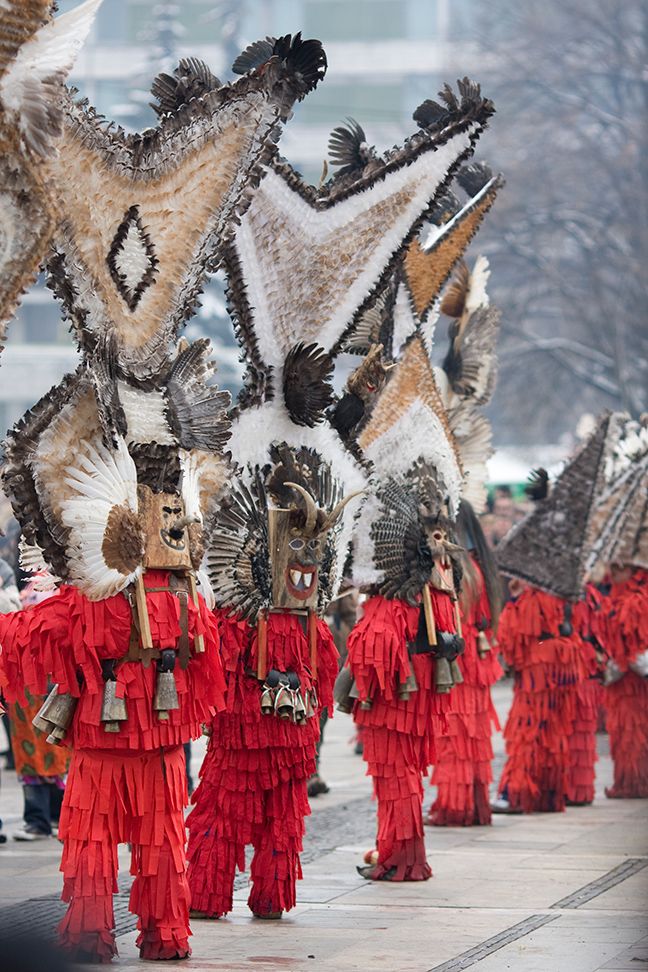 some people are walking down the street in red and black costumes with feathers on them