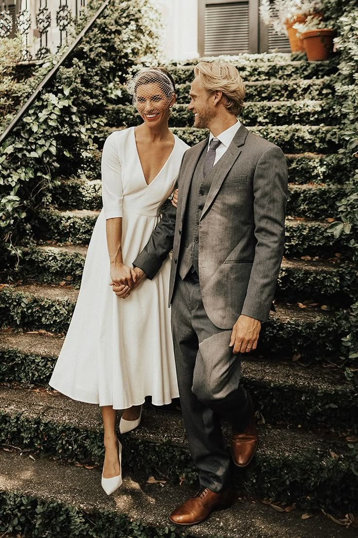 a man and woman standing next to each other in front of some bushes on steps