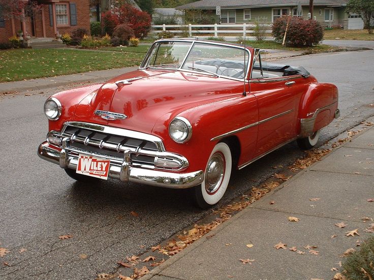 an old red car parked on the side of the road in front of a house