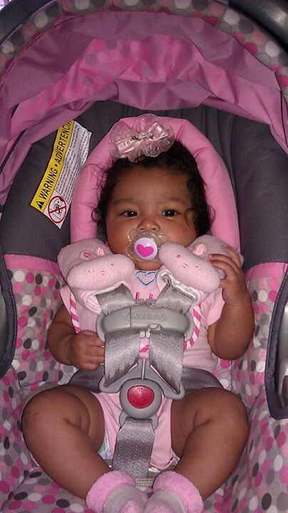 a baby sitting in a car seat with a pacifier in her mouth and wearing a pink outfit