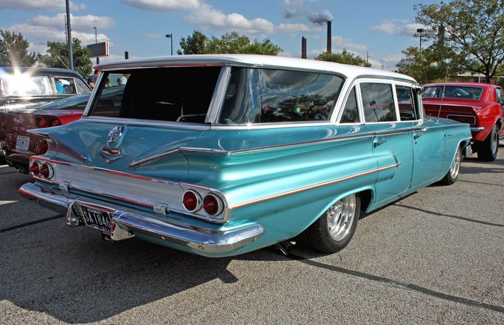 an old blue and white car parked in a parking lot next to other classic cars