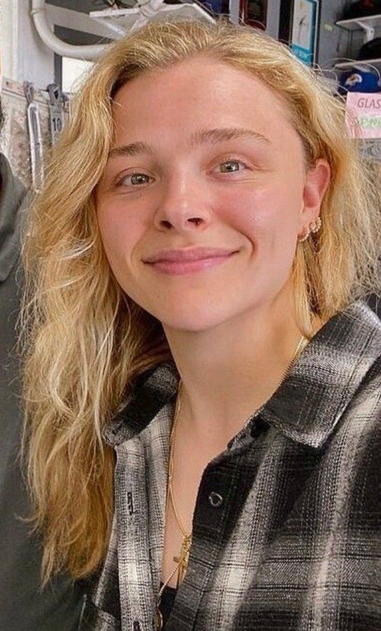 a woman with blonde hair smiling at the camera while standing next to a man in a black and white checkered shirt