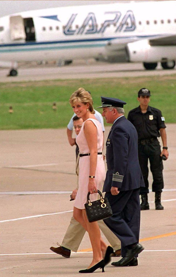 a woman in a white dress walking across an airport tarmac with two uniformed men