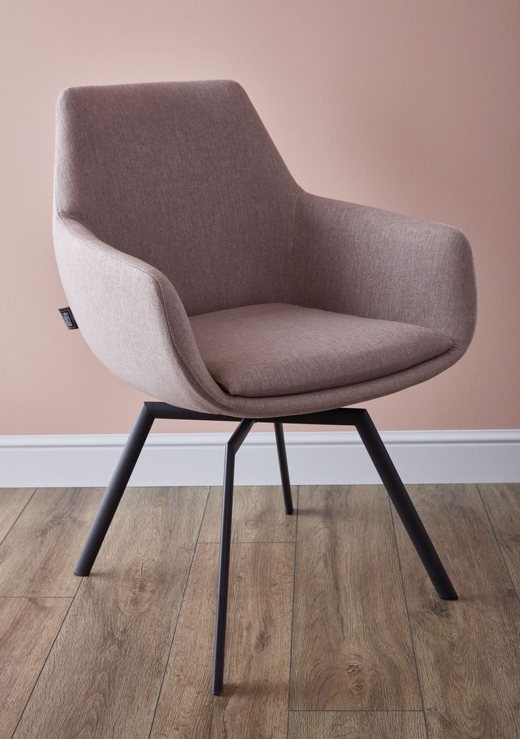 an upholstered chair sits on a wooden floor in front of a pink wall