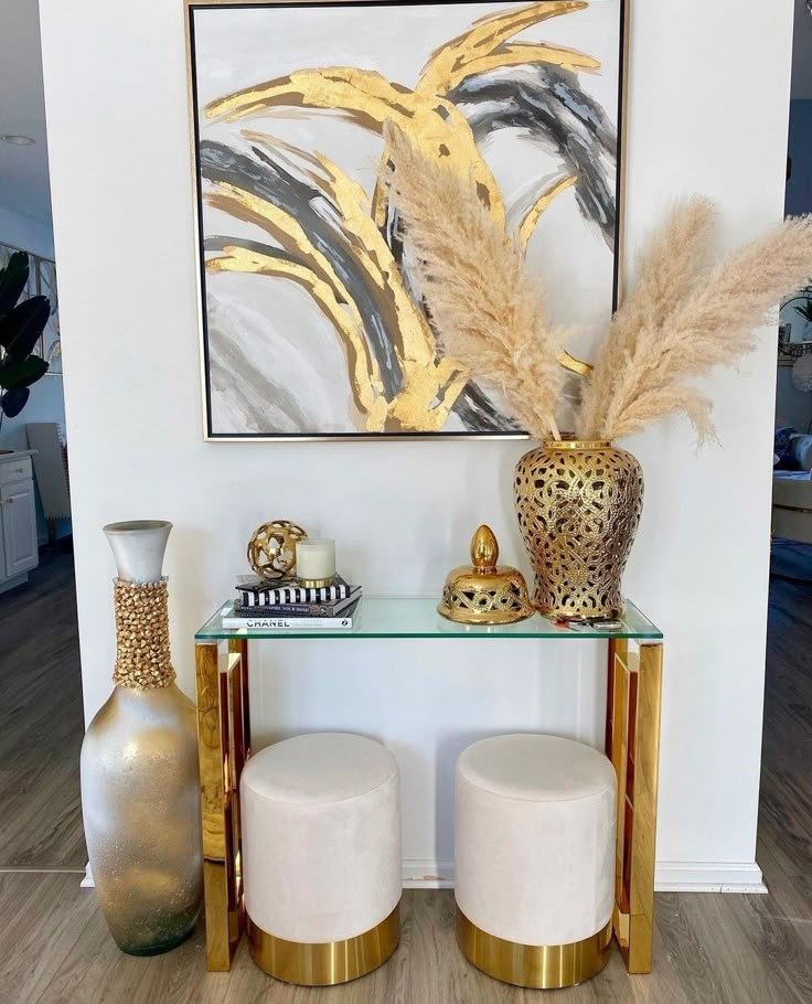 two white stools sitting next to a glass table with vases on top of it