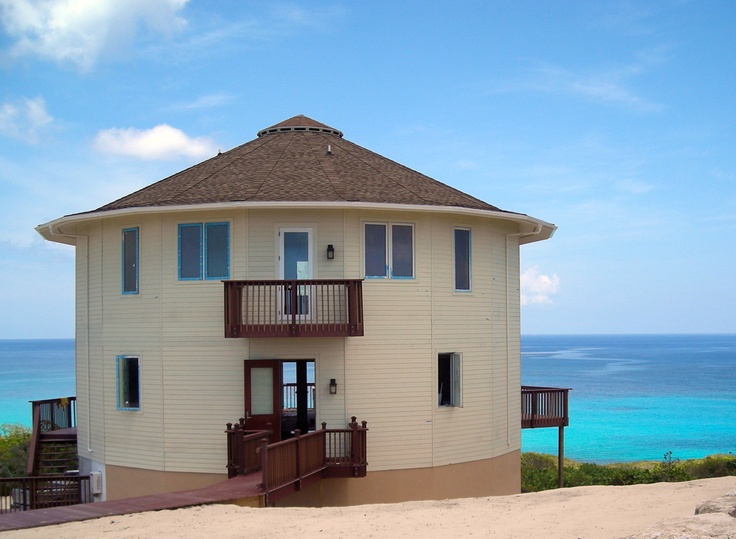 a white building with a brown roof next to the ocean and stairs leading up to it