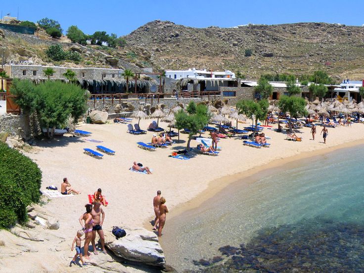 people are on the beach and in the water near some trees, bushes and buildings