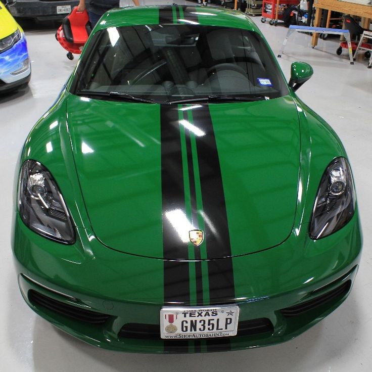 a green sports car with black stripes parked in a garage next to other cars and people