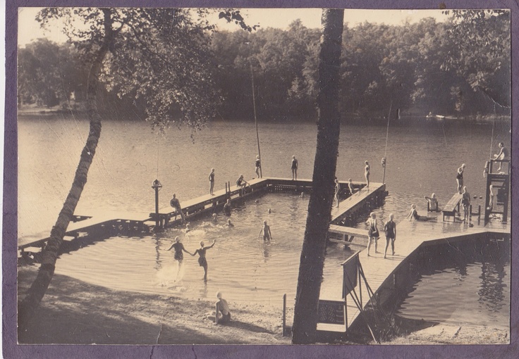 an old black and white photo of people playing in the water at a dock on a lake