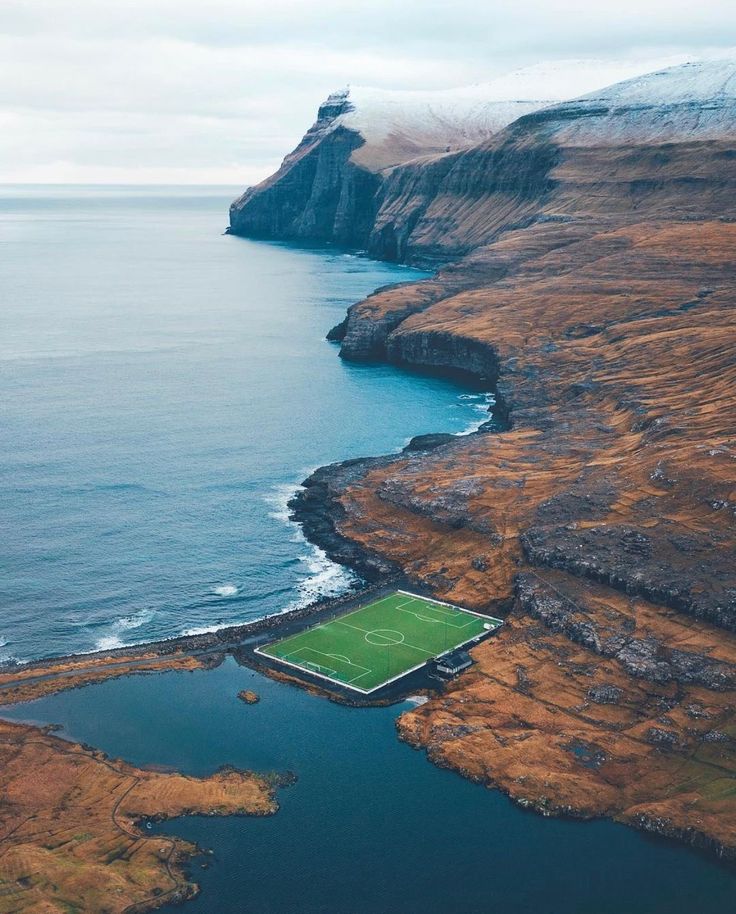 an aerial view of a soccer field in the middle of some water and land with mountains in the background