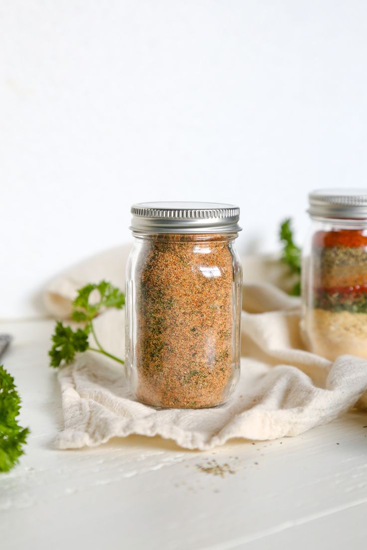 two jars filled with different types of spices on top of a white table next to some parsley