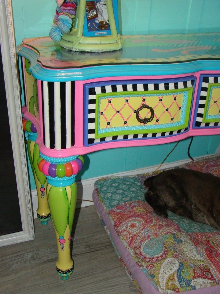 a dog laying on top of a bed next to a colorful desk with drawers and shelves