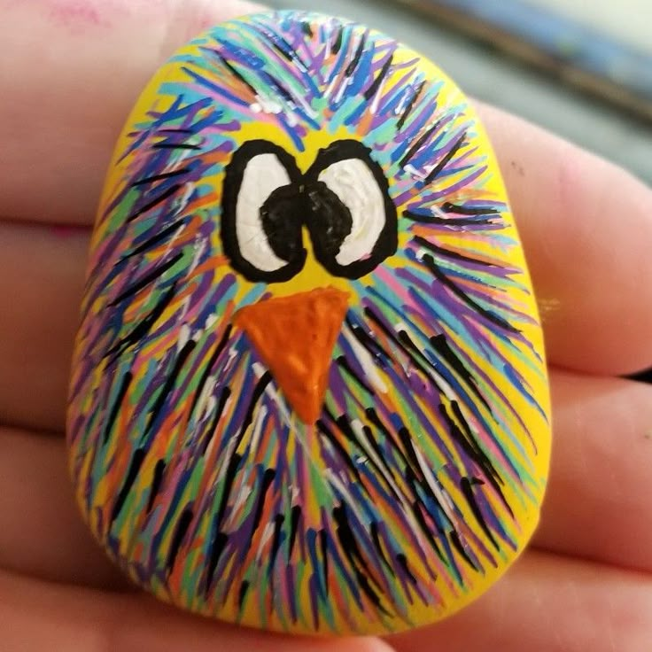 a hand holding a painted rock with an owl face on it