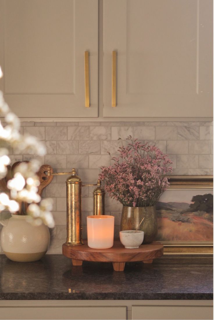 a kitchen counter with candles and vases on top of it in front of white cabinets