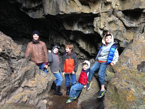 four children are standing on the rocks in front of an entrance to a large cave