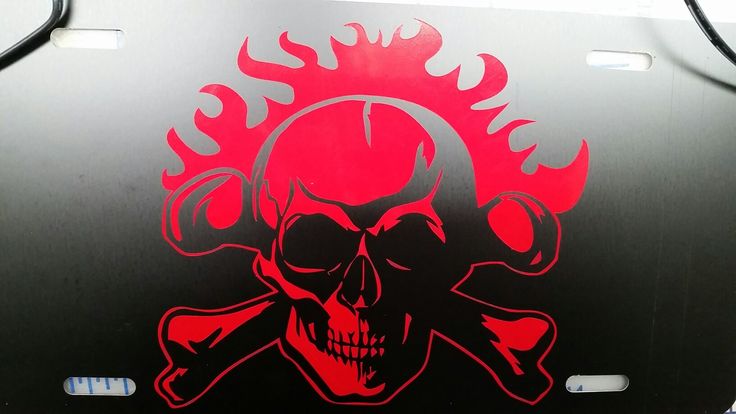 a red skull and crossbones on a black metal license plate that is part of a vehicle