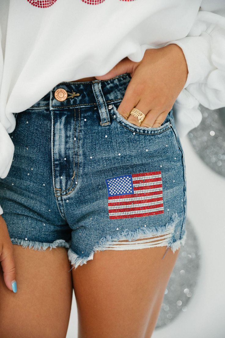 Dress in patriotic style with these USA Patch denim shorts. Featuring a distressed design, a rhinestone American Flag patch, and eye-catching 4th of July detail, these shorts are perfect for the summer months. The perfect combination of style and comfort. All orders are currently shipping within 14 business days. To receive item quicker, expedited shipping is available at checkout. American Flag Clothes, American Flag Shorts, 4th Of July Parade, Patch Denim, American Flag Patch, Patriotic Fashion, Diy Shorts, Flag Patches, Denim Patches