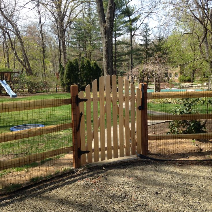 a wooden gate in the middle of a park with a play ground and pool behind it