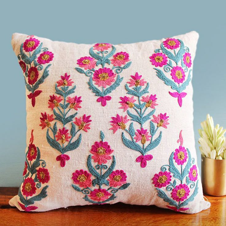 an embroidered pillow on a wooden table next to a succulent potted plant