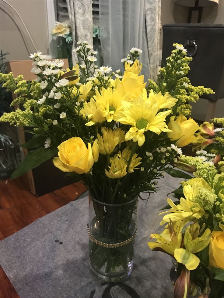 some yellow flowers are in a vase on a table with other flowers and greenery