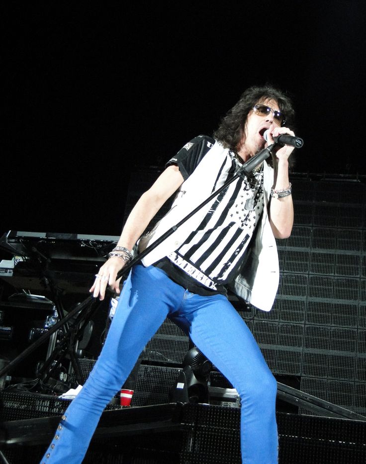 a man standing on top of a stage with a microphone in his hand and wearing blue pants