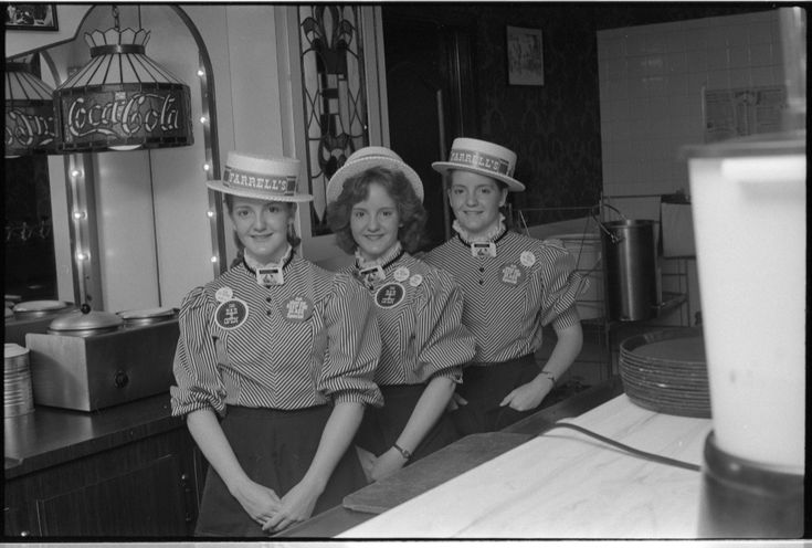 three women in hats are posing for the camera at a restaurant counter with their hands on their hips