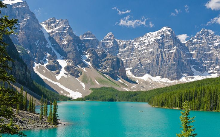 the mountains are covered in snow and green trees near a blue lake with clear water