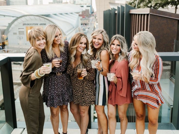 a group of women standing next to each other on top of a balcony holding drinks