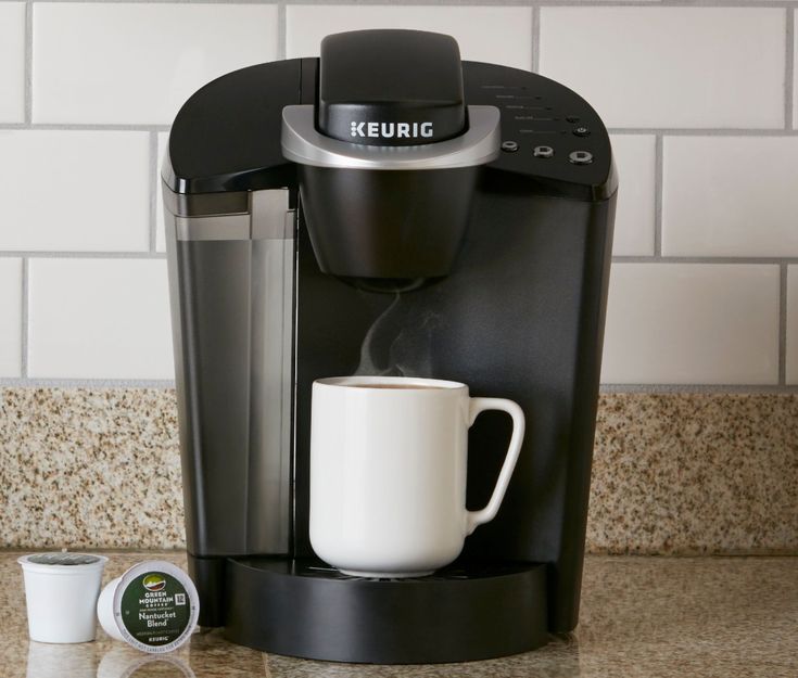 a keurig coffee maker with a white cup on the counter next to it