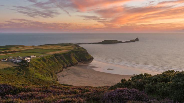 the sun is setting over an ocean and some hills with houses on them in the foreground