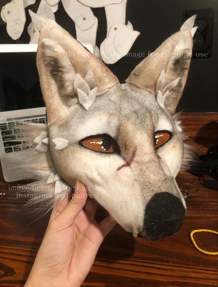 a person holding up a stuffed animal head on top of a wooden table next to a laptop computer