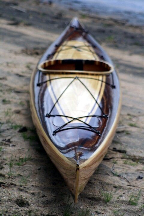 a small wooden boat sitting on top of a sandy beach next to the ocean and grass